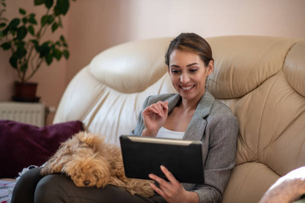 istock Young woman is resting on the sofa bed and using her tablet while her toy poodle is slipping in her lap. 1305647576