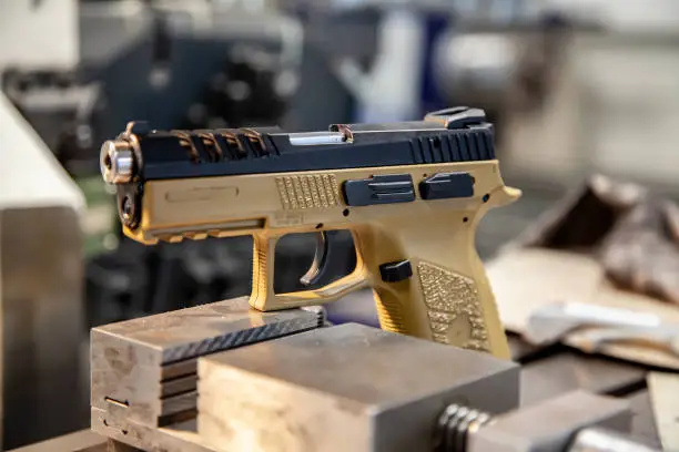 Photo of A modern pistol with a beige grip on a work table in a workshop. Service maintenance of weapons. Pistol repair.