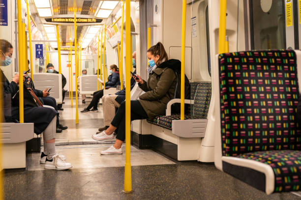 Passengers on a London Underground Tube train using mobile telephones to text during the Coronavirus pandemic in London, England This image depicts a group of passenger wearing masks during the evening rush hour commute in central London Underground Tube using mobile telephones to text during the COVID Coronavirus pandemic - 180 london england rush hour underground train stock pictures, royalty-free photos & images