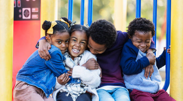 Four young siblings hugging on playground Four siblings sitting at the playground, hugging and smiling at the camera. The oldest is an 8 year old boy. The girl on the left is 5 years old, and the youngest children are 3 year old twins. They are mixed race Hispanic, African-American and Native American. african american children stock pictures, royalty-free photos & images