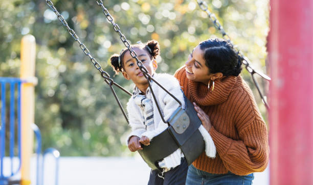 istock Mother with daughter on playground swing 1305651636