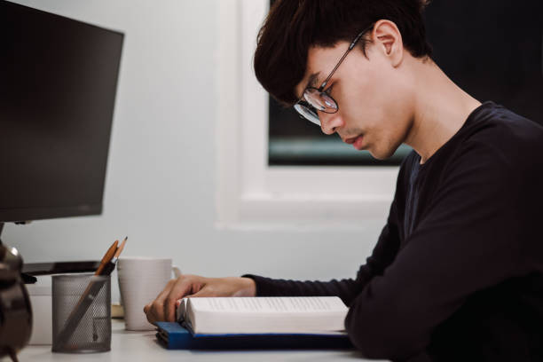 istock Young handsome asian man reading book at work desk late at night, Knowledge and learning concept 1305652701