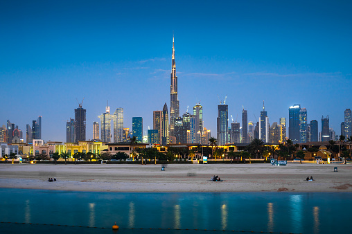 Modern Dubai landmark cityscape view with Jumeirah sandy beach in the foreground at blue hour. United Arab Emirates travel and architecture