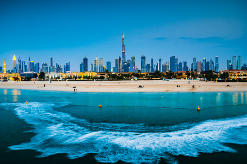 Modern Dubai landmark cityscape view with Jumeirah sandy beach in the foreground at blue hour. United Arab Emirates travel and architecture