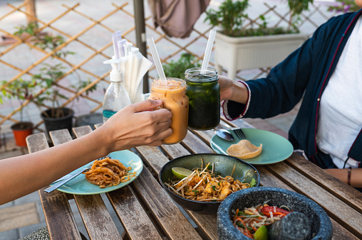 Female friends toasting with Thai milk tea while having a Thai food meal in a restaurant