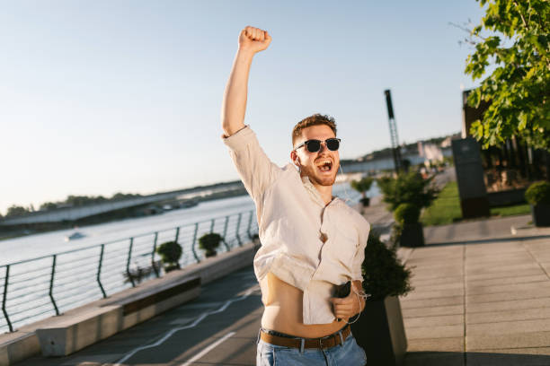 Handsome man holding mobile, listening to music and celebrating outdoors