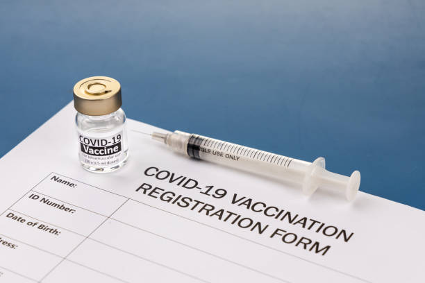 istock Covid-19 vaccination registration form with vial and syringe on blue desk 1305660132