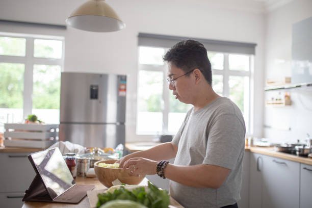 istock Asian Chinese man preparing food in kitchen while using tablet video call. 1305661336