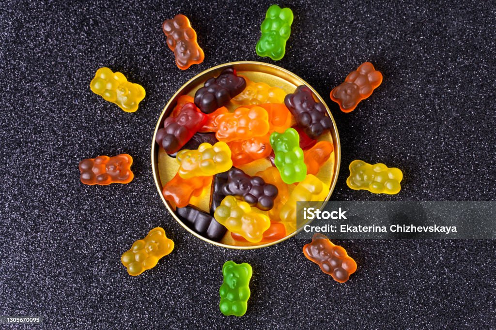 Sun symbol made of multicolored gummy bears Gummy bears arranged in the shape of a sun around a candy box on a sugar coated background. Arranging Stock Photo