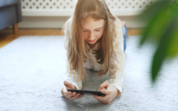 istock Tween girl with smartphone lying on the carpet. 1305670208