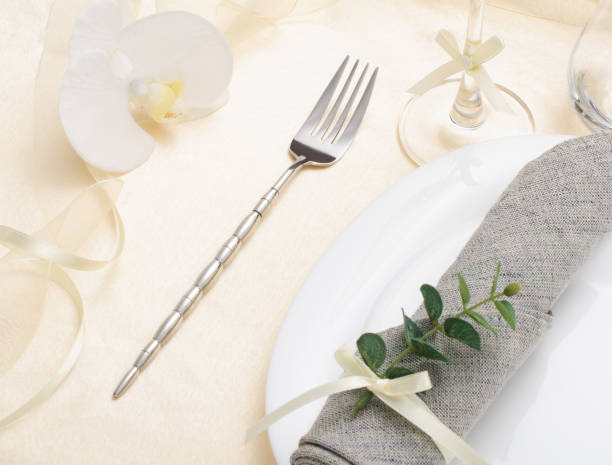 istock Festive romantic table setting with silverware, gray napkin and white crockery on beige silk tablecloth 1305671419
