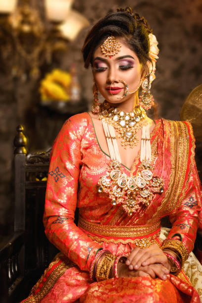 Magnificent young Indian bride in luxurious bridal costume with makeup and heavy jewellery is sitting in a chair in with classic vintage interior in studio lighting. Wedding fashion. Magnificent young Indian bride in luxurious bridal costume with makeup and heavy jewellery is sitting in a chair in with classic vintage interior in studio lighting. Wedding fashion. hairstyle bride jewelry women stock pictures, royalty-free photos & images
