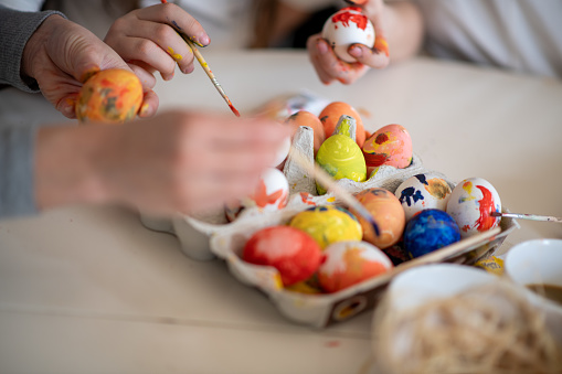 Hands painting on eggs. In egg carton are boiled eggs in different colors, drying. There are yellow, red, blue, orange, spotted, and multi-colored eggs. Close up.