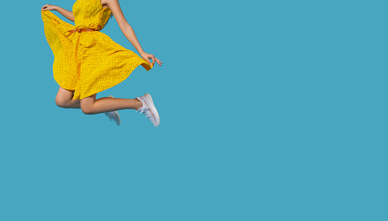 Girl with yellow dress jumping in the air isolated on blue background. Life people energy concept. High quality photo