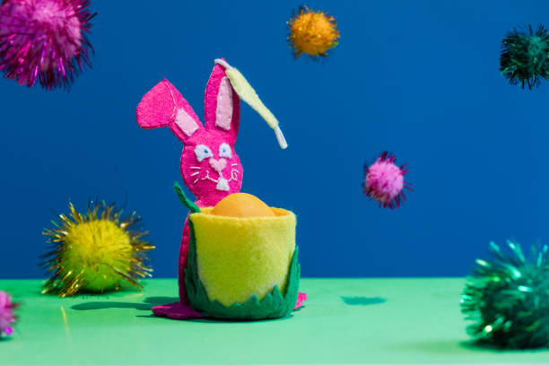 istock Easter happy felt pink rabbit with protective mask on his ear is on the blue with levitate colored balls  background. Creative coronavirus Eastern concept . 1305674475