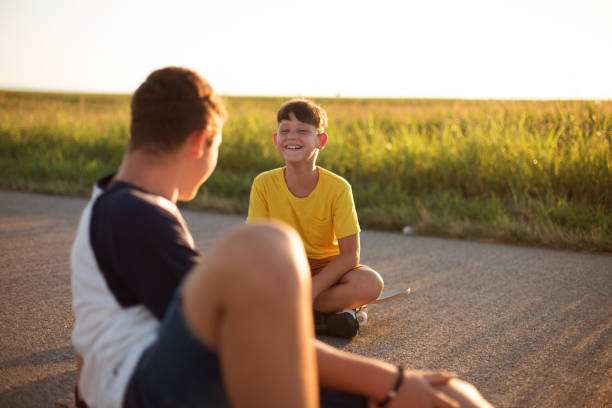 istock Two boys resting and sitting on skate boards, talking and joking. 1305681457