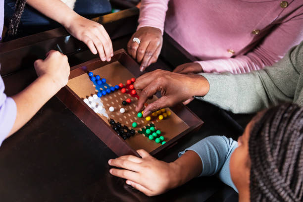 Cropped view of family playing chinese checkers Cropped view of an African-American family playing chinese checkers. The game board is in the middle, with hands surrounding it. Father is moving one of the game pieces. chinese checkers stock pictures, royalty-free photos & images