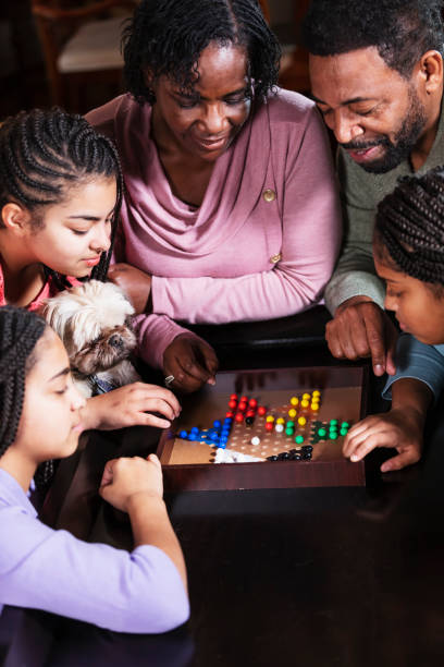 African-American family at home playing chinese checkers An African-American family with three teenage daughters spending time together at home. It is game night, and they are sitting around the living room coffee table playing chinese checkers. The parents are in their 50s, and the girls are 13, 14 and 16 years old. chinese checkers stock pictures, royalty-free photos & images