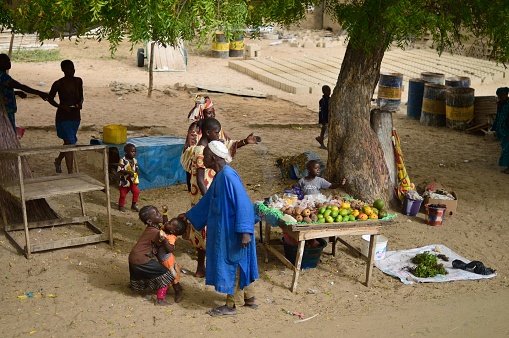 Dakar, Senegal - May 21,2012 : A vegetable and fruit stand near Lake Retba, Lac Rose, with a Senegal family, looks like Mom, teenage daughter, elementary school age children, several pre-school age children and a toddler bringing up the read and  an older man playing with a toddler