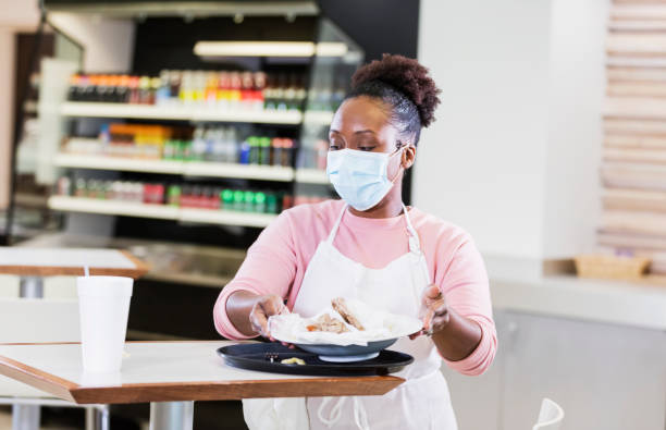istock Waitress in diner cleaning a table, wearing mask 1305686693