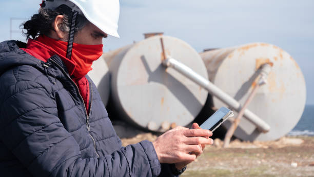 brennstoff- und stromerzeugungssysteme-ölfeld. wartungsingenieur trägt schutzbeschützende gesichtsmaske während der arbeit auf dem feld in einem erdölkraftwerk während der covid-19-pandemie. - storage tank storage compartment fuel and power generation oil industry stock-fotos und bilder