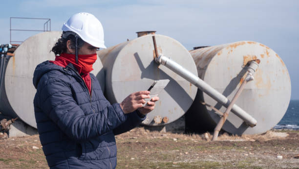 brennstoff- und stromerzeugungssysteme-ölfeld. wartungsingenieur trägt schutzbeschützende gesichtsmaske während der arbeit auf dem feld in einem erdölkraftwerk während der covid-19-pandemie. - storage tank storage compartment fuel and power generation oil industry stock-fotos und bilder