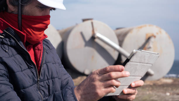 brennstoff- und stromerzeugungssysteme-ölfeld. wartungsingenieur trägt schutzbeschützende gesichtsmaske während der arbeit auf dem feld in einem erdölkraftwerk während der covid-19-pandemie. - storage tank storage compartment fuel and power generation oil industry stock-fotos und bilder