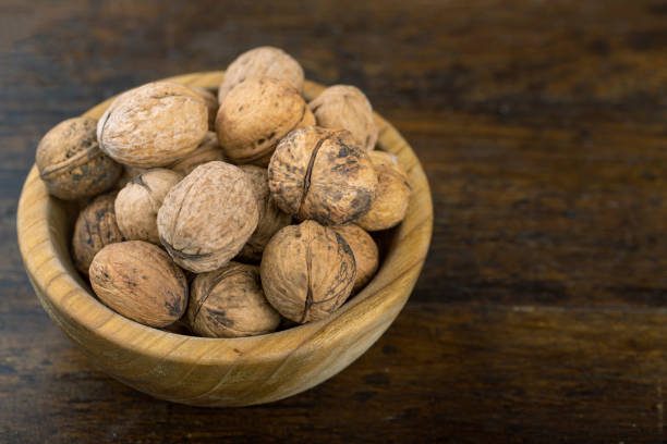 istock Walnut in wooden bowl on black background with copy space. 1305693173
