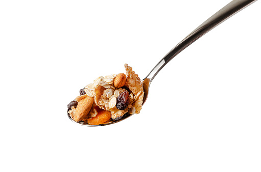 Metal spoon with fiber flakes, oats,almond and dried fruits. Isolated on white background.