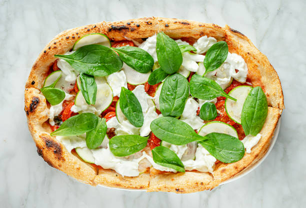 istock Roman pizza with spinach, zucchini slices, stracciatella cheese and tomatoes on marble background.. Italian food 1305699239
