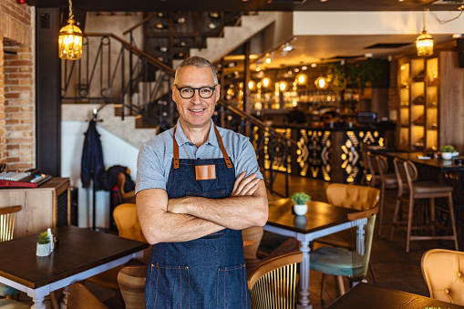 Proud, mature café owner with apron standing on the door of café and looking at camera, smiling