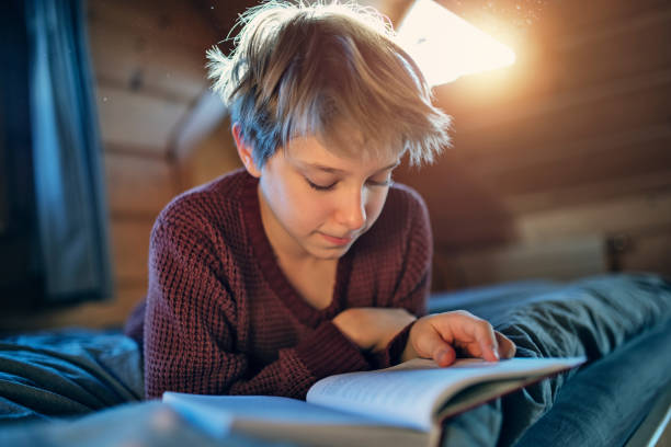 istock Teenage boy reading a book on the bed 1305703349