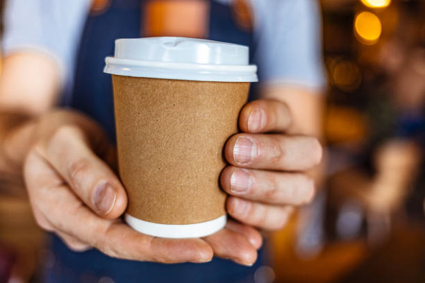 Your take-away coffee is ready! Photo of waiter holding and serving a paper cup of hot coffee paper coffee cup stock pictures, royalty-free photos & images