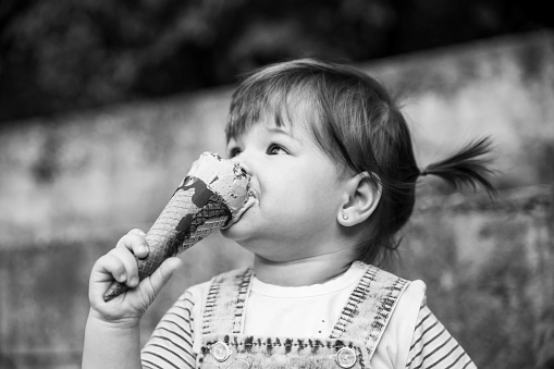 Small toddler girl enjoying eating ice cream outdoor