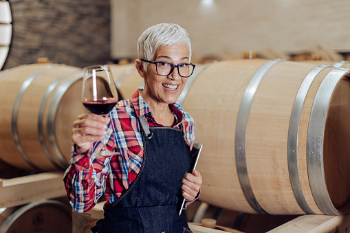 Portrait of a female senior entrepreneur working at her winery and toasting with wine.