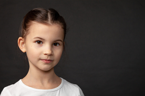 close up studio portrait of 8 year old girl with brown hair back in white t-shirt on black background