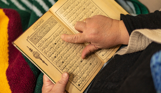 Hand detail with the old woman reading the Koran and the Quran.