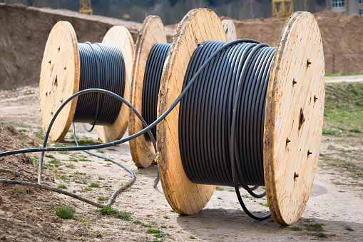 Concept of electricity supply for construction projects. Several wooden coils with power cable, laid in trench.