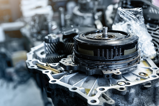 Closeup disassembled car automatic transmission gear part on workbench at garage or repair factory station for fix service or maintenance. Vehicle part detail. Complex industrial mechanism background.