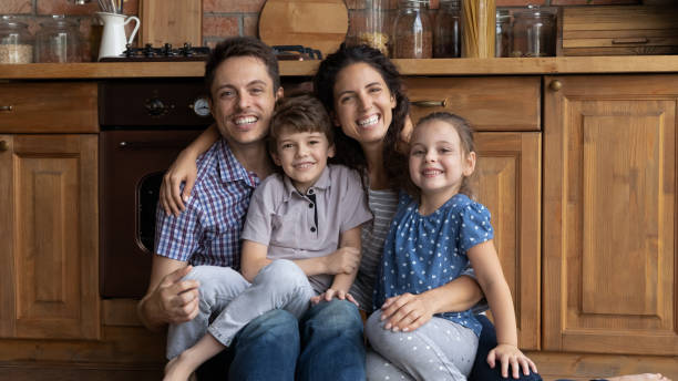 porträt überglückliche eltern mit kindern, die auf warmem küchenboden sitzen - small domestic kitchen apartment rental stock-fotos und bilder