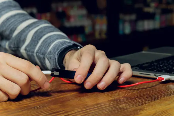 Photo of POD e-cigarette or nicotine vapor dispenser being charged in modern laptop with Pods.