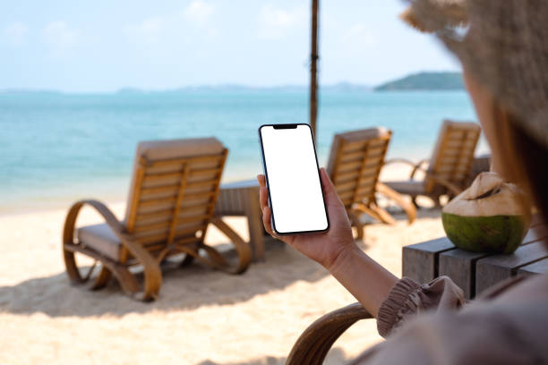 istock a woman holding mobile phone with blank desktop screen while sitting on the beach 1305738743