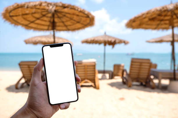istock a man holding mobile phone with blank desktop screen while sitting on the beach 1305738754