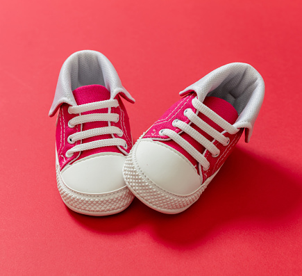 Booties baby sport shoes red and white color on red color background. Kid small size sneakers, canvas booties with shoelace closeup view. Children first steps.