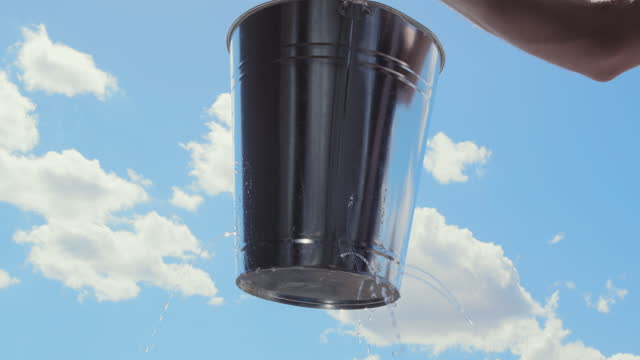 Man lifts Leaking bucket with water dripping, blue sky clouds, Lost opportunity