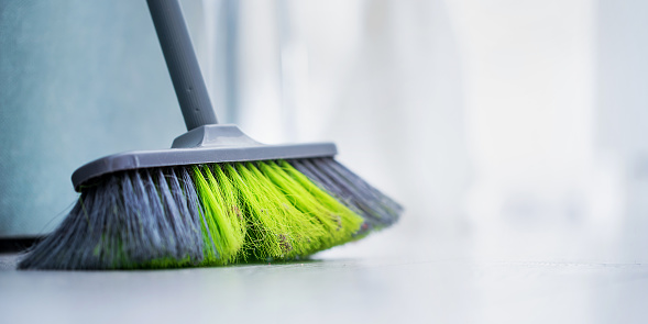 Big broom with green hair stands on wooden office or home floor for cleaning room closeup