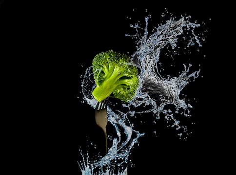 Broccoli on fork with water splash or explosion flying in the air isolated on black background. Nutrition and diet picture.