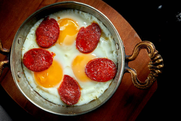 istock Appetizing turkish breakfast dish - scrambled eggs with sujuk in a frying pan on a black background 1305760996