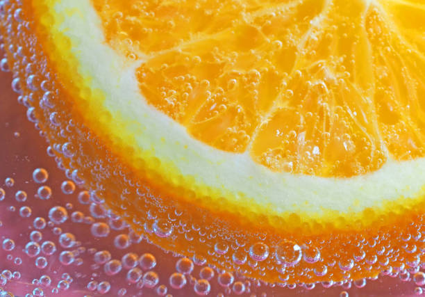 Cut round a piece of orange orange in bubbles of carbonated water on pink background abstract background horizontal image of free space to text summer freshness vitamins healthy diet food