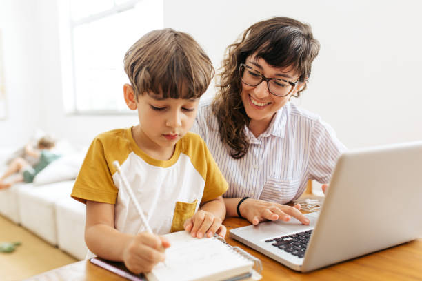 Boy doing homework with mother working Boy writing on a book while his mother working on laptop. Kid studying with mother working from home. homework stock pictures, royalty-free photos & images